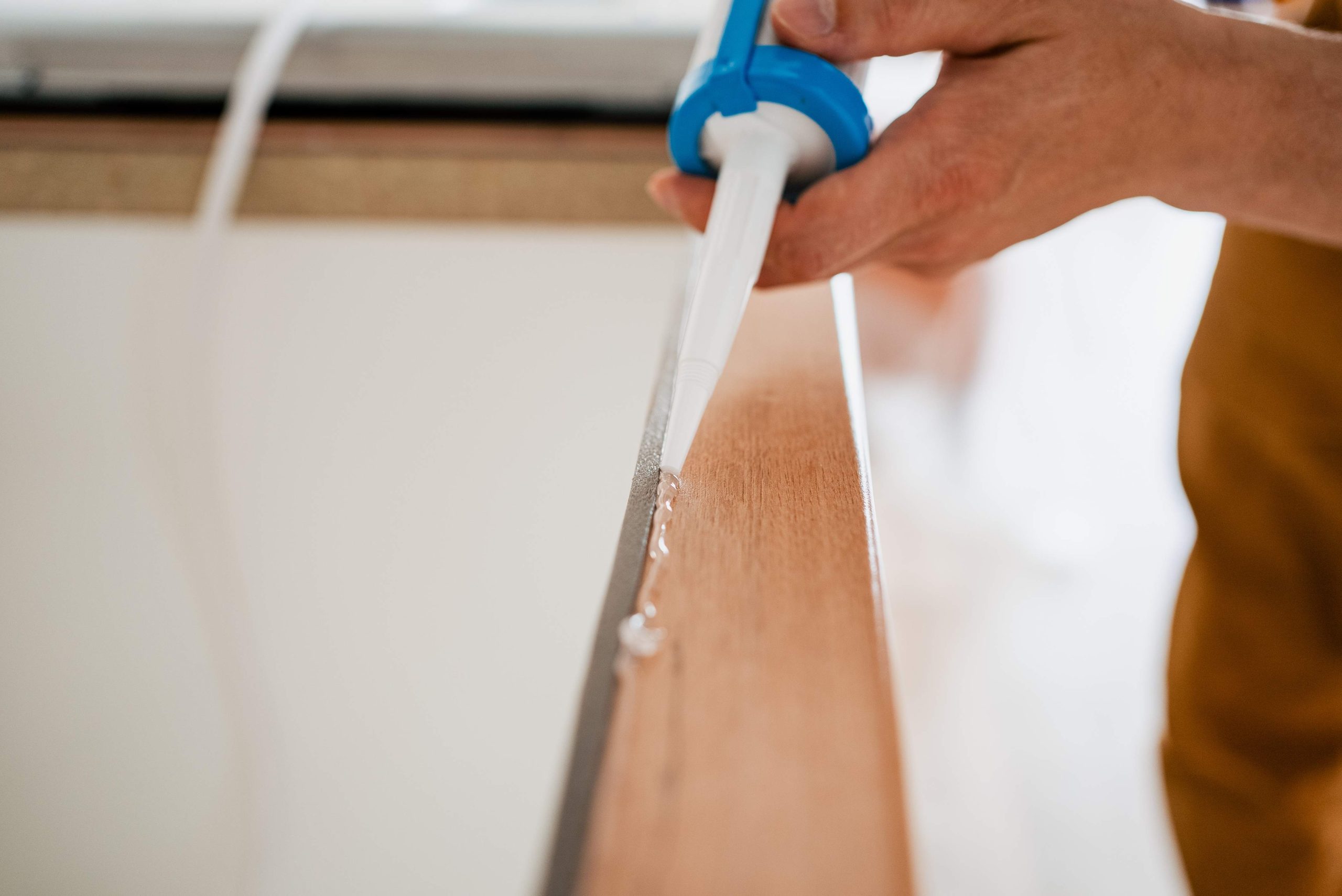 Construction worker sealing wooden plank with silicone using caulking gun, creating waterproof barrier during home repair and renovation project