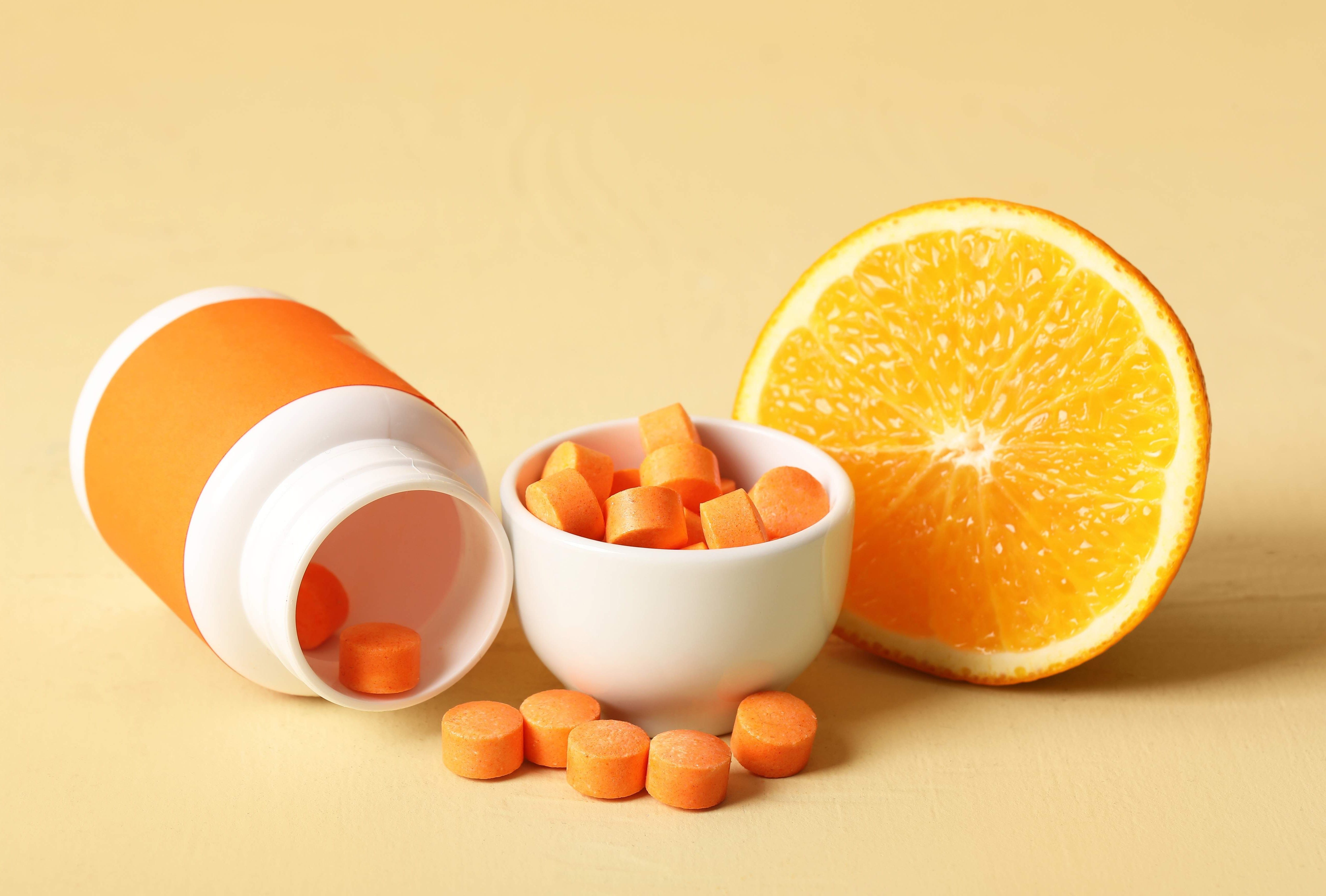Bottle and bowl with vitamin C pills on beige background with space for text